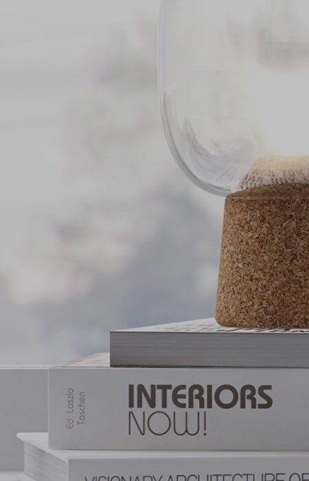 A glass container with a cork stopper resting atop a hardcover book titled "interiors now!" with a blurred background suggesting a tranquil and stylish living or workspace.
