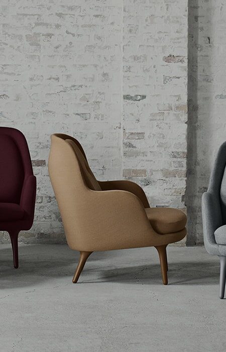 Three modern armchairs in maroon, tan, and gray colors set against an industrial backdrop with a white brick wall.
