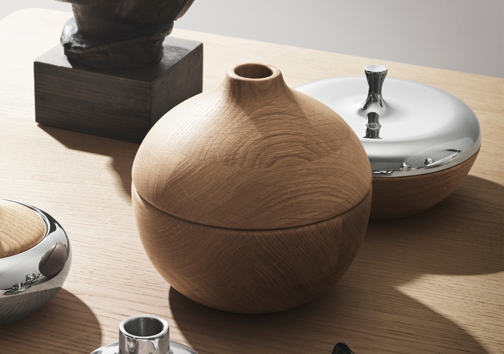 Elegant home decor arrangement featuring a wooden spherical vase, a sleek bowl with a silver lid, and a combination of polished metallic and rustic wooden accessories on a smooth tabletop.